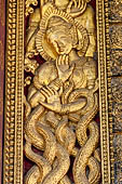 Wat Xieng Thong temple in Luang Prabang, Laos. Detail of a wooden door of the sim with gilded carvings on a red background. 